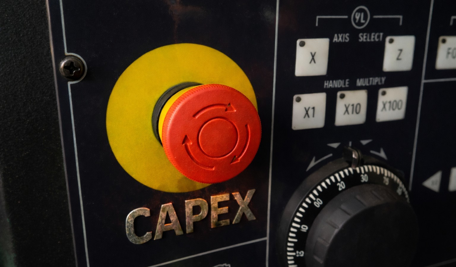 Botón de parada de emergencia en un panel CNC con la palabra CAPEX, simbolizando una decisión de inversión forzada por una avería electrónica.